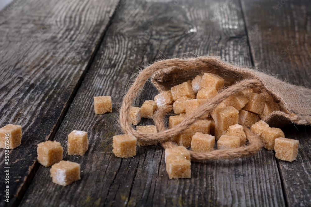 Fototapeta premium Many pieces of brown sugar on a wooden background. Heap of brown sugar cubes on wooden table, closeup