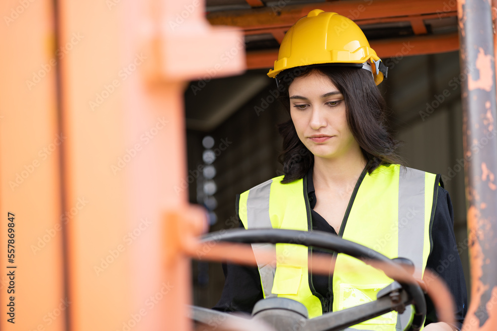 Female foreman wears hard hat driving forklift at shipping container ...