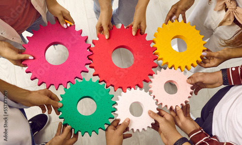 Students or business people joining gears. Team of men and women standing in circle and holding colorful cogs. Cropped shot. Teamwork, integration, business, education, success concept background