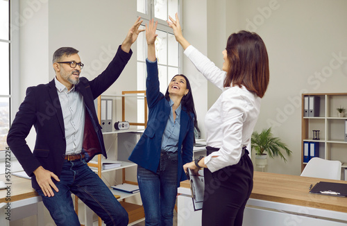Happy successful business team giving high five celebrating achievement. Coworkers raising their hand cheering teamwork results in office. Team building, corporate meeting and unity