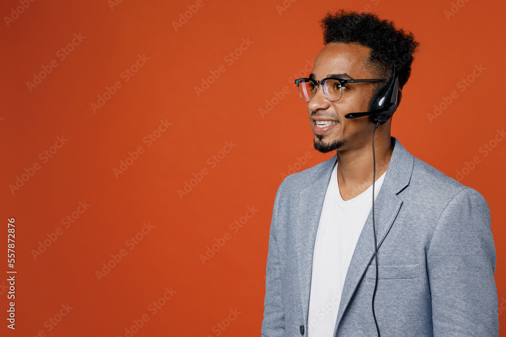 Side view happy employee operator business man in set microphone headset for helpline assistance work at call center office look aside on workspace area isolated on plain red orange background studio. - obrazy, fototapety, plakaty 