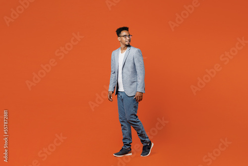 Full body side view young employee business man corporate lawyer wear classic formal grey suit shirt glasses work in office look aside on workspace go isolated on plain red orange background studio.