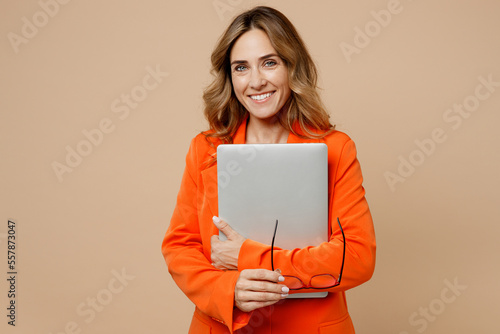 Foto Young happy successful employee IT business woman corporate lawyer 30s wearing classic formal orange suit glasses work in office hold use laptop pc computer glasses isolated on plain beige background