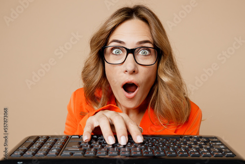 Close up young successful employee business woman corporate lawyer 30s wear classic formal orange suit glasses work in office typing on pc computer keyboard isolated on plain beige background studio. photo