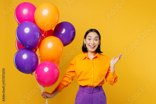 Happy fun surprised shocked young woman wearing casual clothes celebrating holding bunch of colorful air balloons spread hands isolated on plain yellow background. Birthday 8 14 holiday party concept.