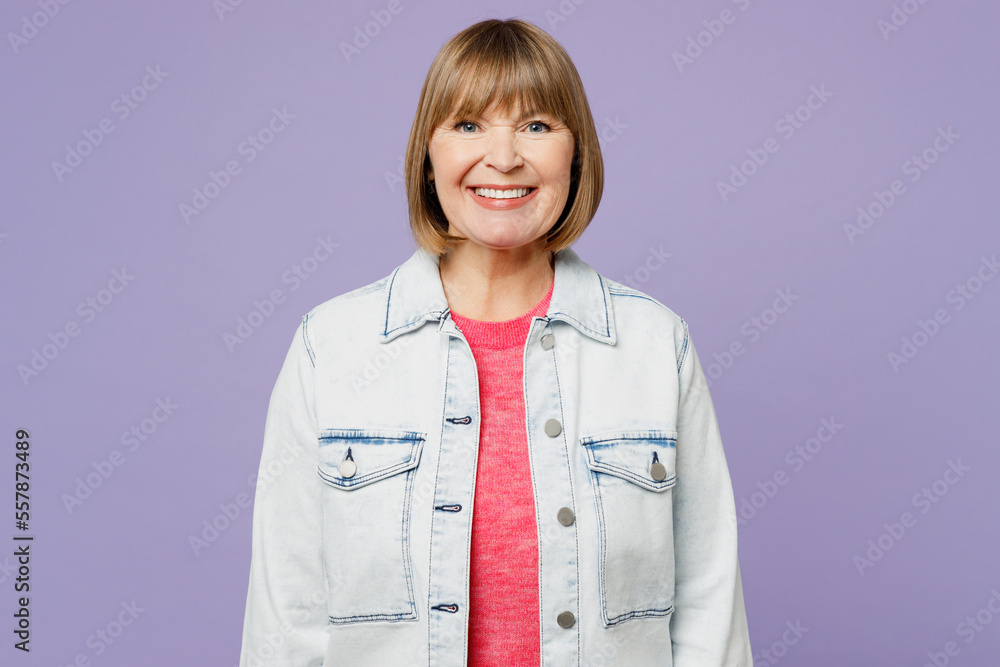 Elderly smiling happy fun cheerful blonde satisfied woman 50s years old she wearing casual clothes denim jacket t-shirt looking camera isolated on plain pastel light purple background studio portrait. Elderly smiling happy fun cheerful blonde satisfied woman 50s years old she wearing casual clothes denim jacket t-shirt looking camera isolated on plain pastel light purple background studio portrait.