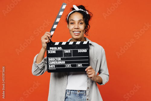 Young woman of African American ethnicity she wear grey shirt headband hold in hand classic black film making clapperboard isolated on plain orange background studio portrait People lifestyle concept © ViDi Studio