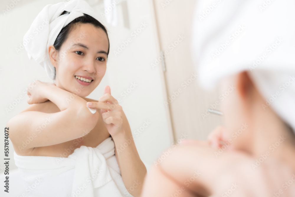 Happy young Asian woman applying lotions on her body in bathroom