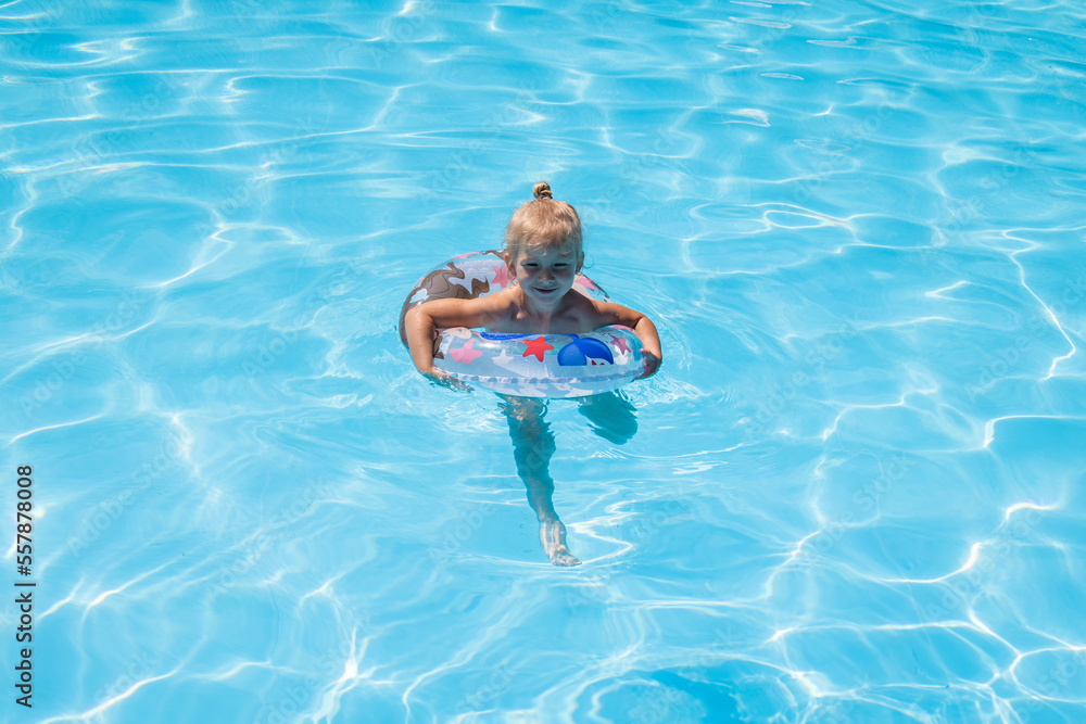 Blonde child girl is played swimming with an inflatable ring in a summer pool