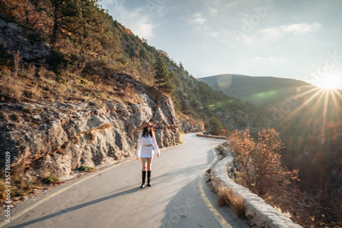 The woman is dear to the mountains. A woman in a white sweater, black boots and a hat walks along a winding alpine path between the mountains at the end of summer at sunset. Travel concept. photo