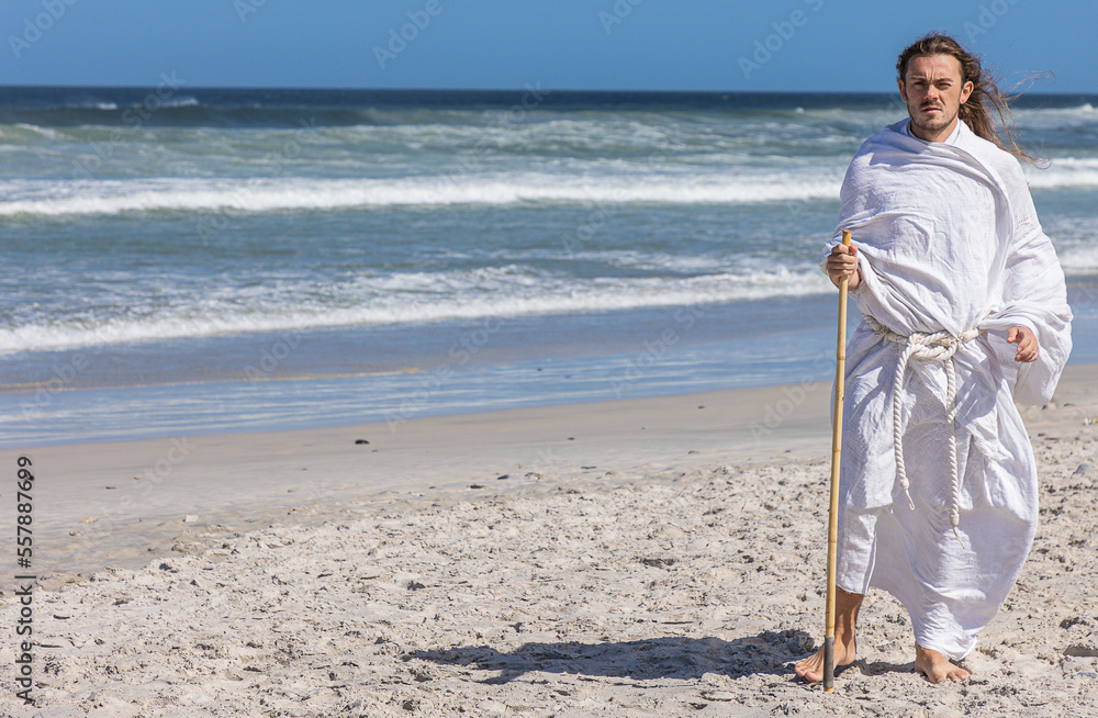 Handsome bearded man in white robe, (portrait) with staff walks next to sea