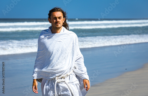 Obraz na płótnie Bearded, handsome man in white robe (resembles Christ) walking next to sea w salonie