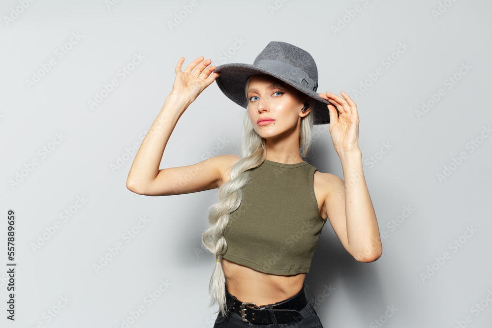 Studio portrait of happy pretty blonde girl with wireless earphones into ears adjusts her hat, on white background. Studio portrait of happy pretty blonde girl with wireless earphones into ears adjusts her hat, on white background.