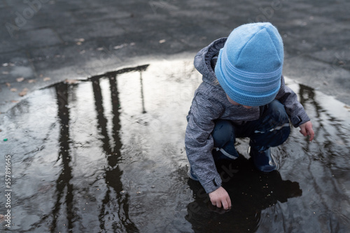 two year old boy in rain pants and rubber boots playing in puddle of water after rain shower