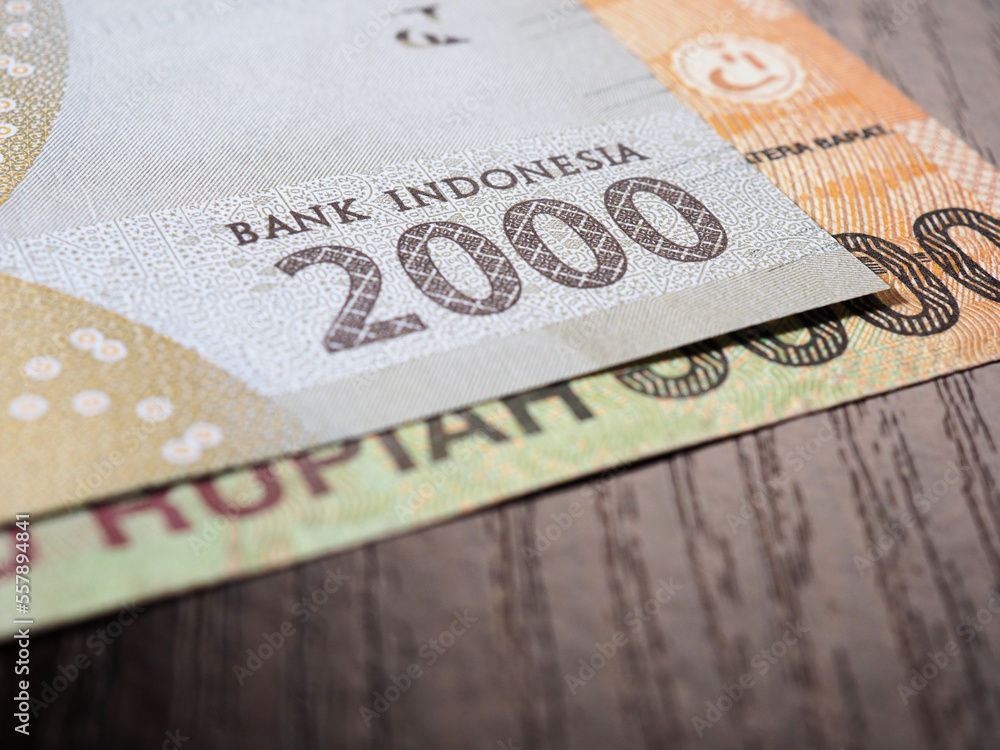 Obraz premium Indonesian banknotes lie on dark surface of office table. Fragment of 2000 rupiah note. Illustration on theme of economics or banking. Money of Indonesia. News about exchange rate or inflation. Macro