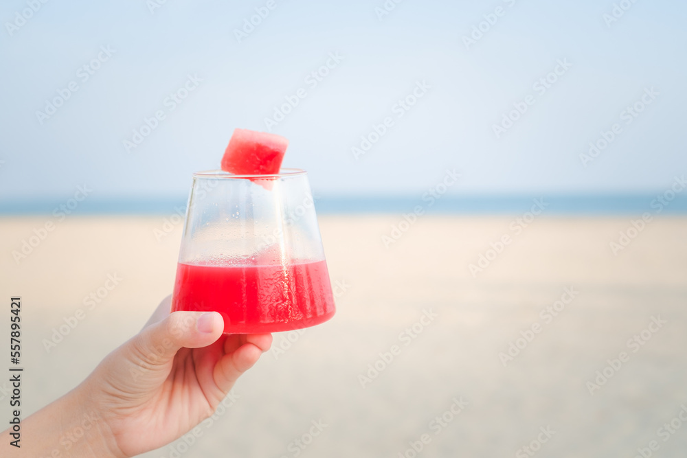 hand holding a glass of watermelon smoothie cocktail by the sea with blue sky background on tropical beach. hand holding a glass of watermelon smoothie cocktail by the sea with blue sky background on tropical beach.