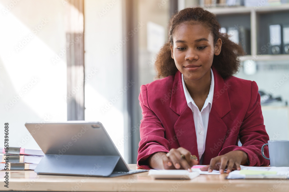 Fototapeta premium Young african american businesswoman red suit working at desk and using digital tablet in the modern office. Start up SME worker concept.