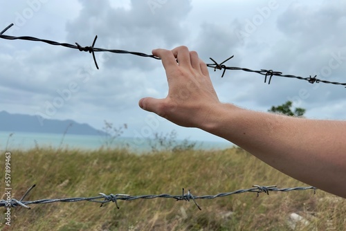 a hand holds on to barbed wire against a stormy sky. man seeks freedom behind the fence. 