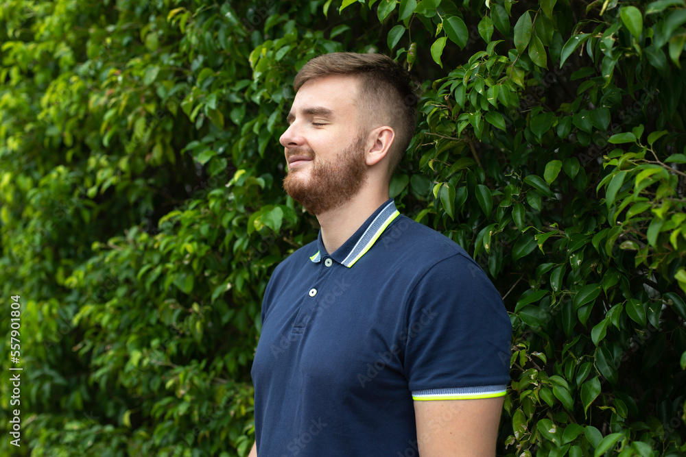 Portrait of a beautiful young bearded man with beard standing on an Ivy wall or in greenery, smiling against from plant, guy relaxing outdoors at sunny summer day. Love nature, eco life Portrait of a beautiful young bearded man with beard standing on an Ivy wall or in greenery, smiling against from plant, guy relaxing outdoors at sunny summer day. Love nature, eco life