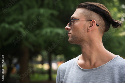 Handsome young man in stylish sunglasses at park, space for text