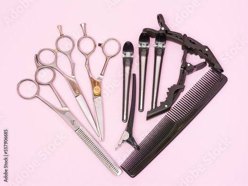 Composition of hairdressing scissors for cutting and thinning, hair clips and a comb in the form of a heart on a pink background. Provision of hairdressing services. Tools for hair lovers. Top view