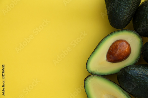 Fresh whole and cut avocados on yellow background, flat lay. Space for text