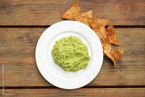 Delicious guacamole made of avocados and nachos on wooden table, flat lay