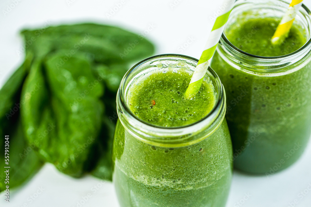 Closeup top view of glasses jars with straws filled with green smoothie and spinach on the table Closeup top view of glasses jars with straws filled with green smoothie and spinach on the table