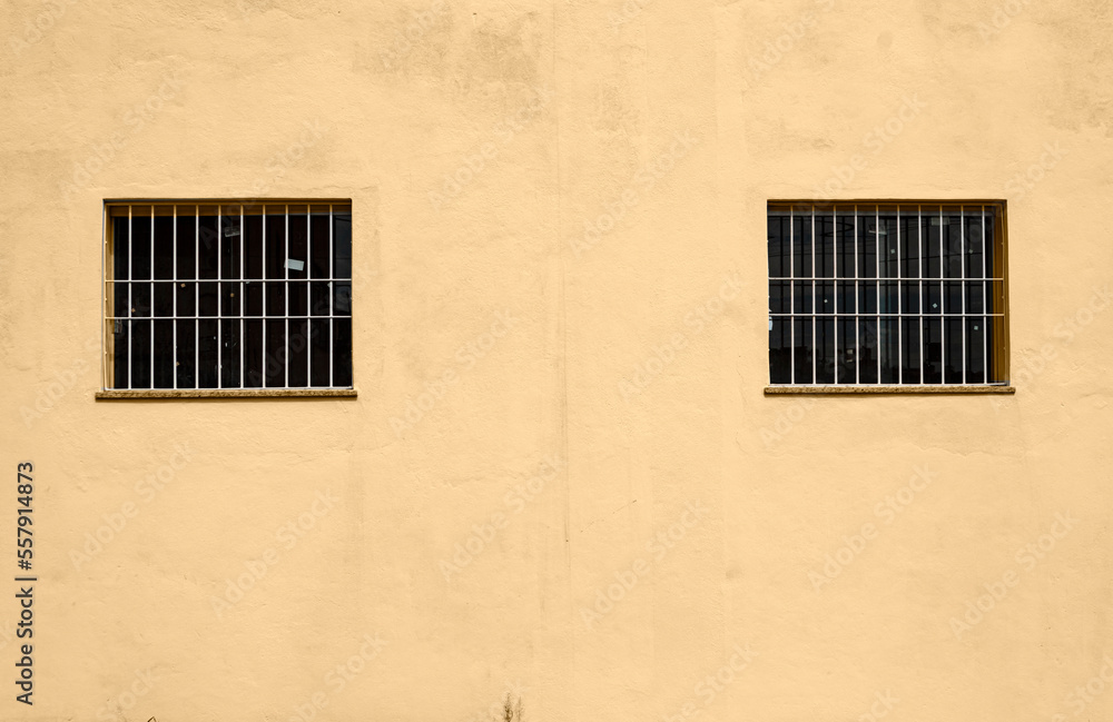 External yellow wall with two small windows with bars.