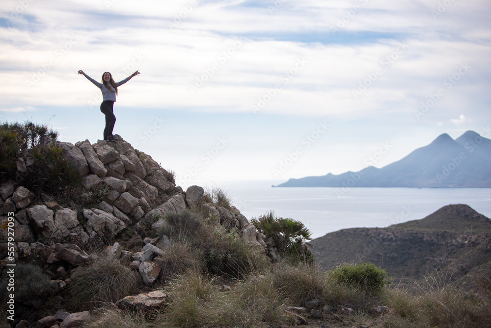 young woman standing on top of a mountain staring at the sea