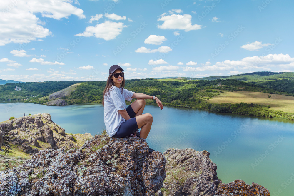 Young traveler woman sitting on a rocks above blue lake .Traveling in the summer nature in Bulgaria	. Pchelina Lake 