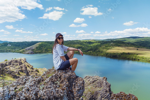 Young traveler woman sitting on a rocks above blue lake .Traveling in the summer nature in Bulgaria	. Pchelina Lake  photo