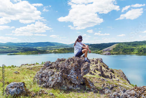 Young traveler woman sitting on a rocks above blue lake .Traveling in the summer nature in Bulgaria	. Pchelina Lake  photo