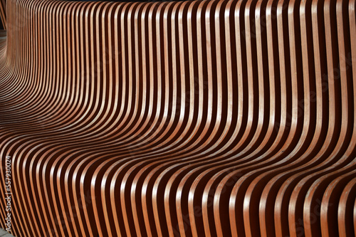 Wooden brown curved slats. Beautiful reflections of the sun on the surface of the bench element. Abstract background.