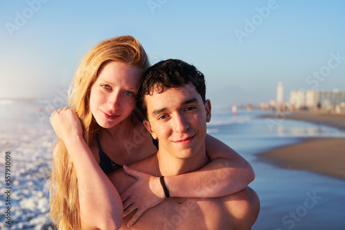 portrait young Argentinian couple in piggyback position smiling looking at camera on the shore of the beach 