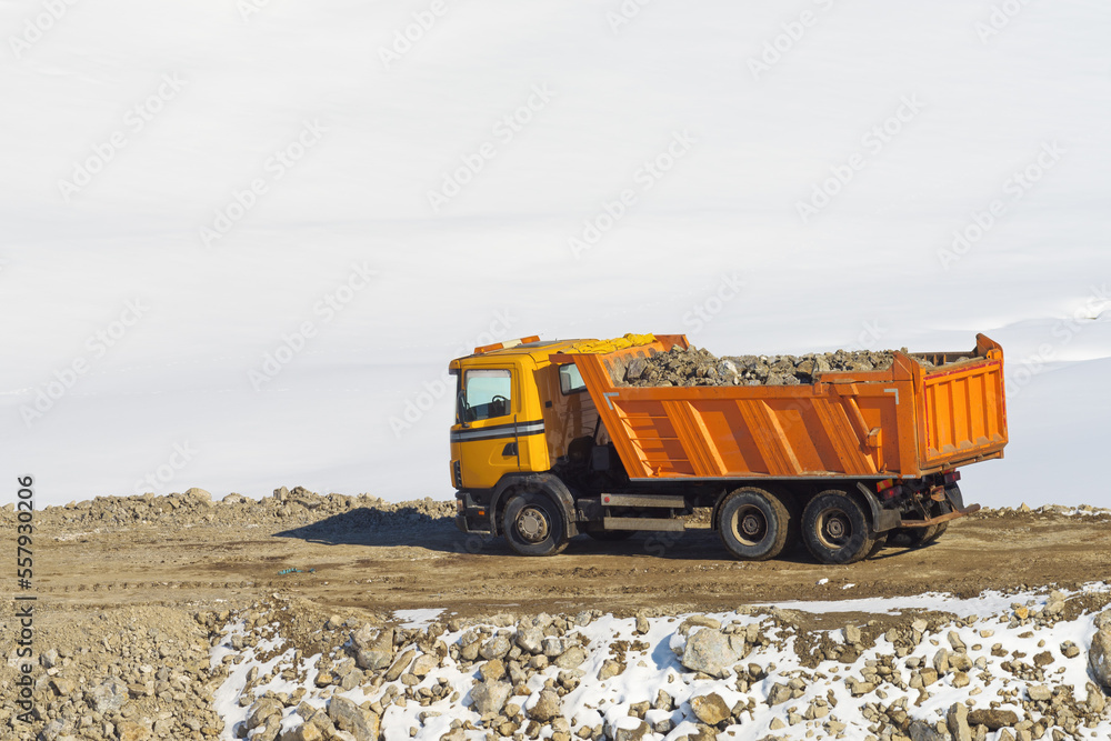 Obraz premium Industrial dump truck with trailer loaded with stones and rubble on road building construction site covered with snow in winter on Zlatibor mountain in Serbia