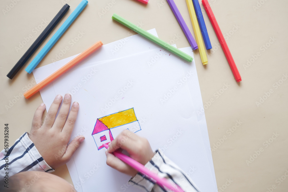 top view of child girl drawing a house with color pencils on paper top view of child girl drawing a house with color pencils on paper