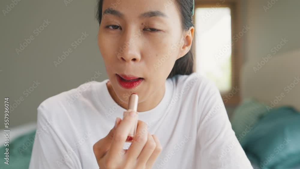 Young happy Asia girl beauty blogger look at camera makeup apply lipstick balm on her lips in bedroom. Lifestyle and people, Make up Natural look, Skin Care Cosmetics, Morning routine concept. Young happy Asia girl beauty blogger look at camera makeup apply lipstick balm on her lips in bedroom. Lifestyle and people, Make up Natural look, Skin Care Cosmetics, Morning routine concept.