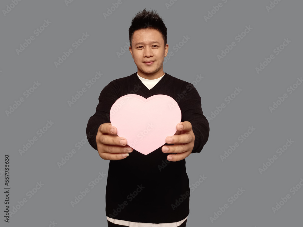 handsome man holding or giving heart shaped gift box with smiling expression looking at camera handsome man holding or giving heart shaped gift box with smiling expression looking at camera