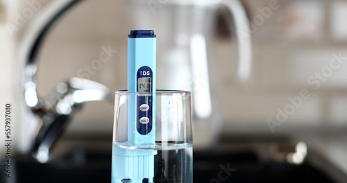 Measurement of TDS of water. Electronic pH meter in a glass of water.Filter for water purification. There is a tap for drinking water in the background.