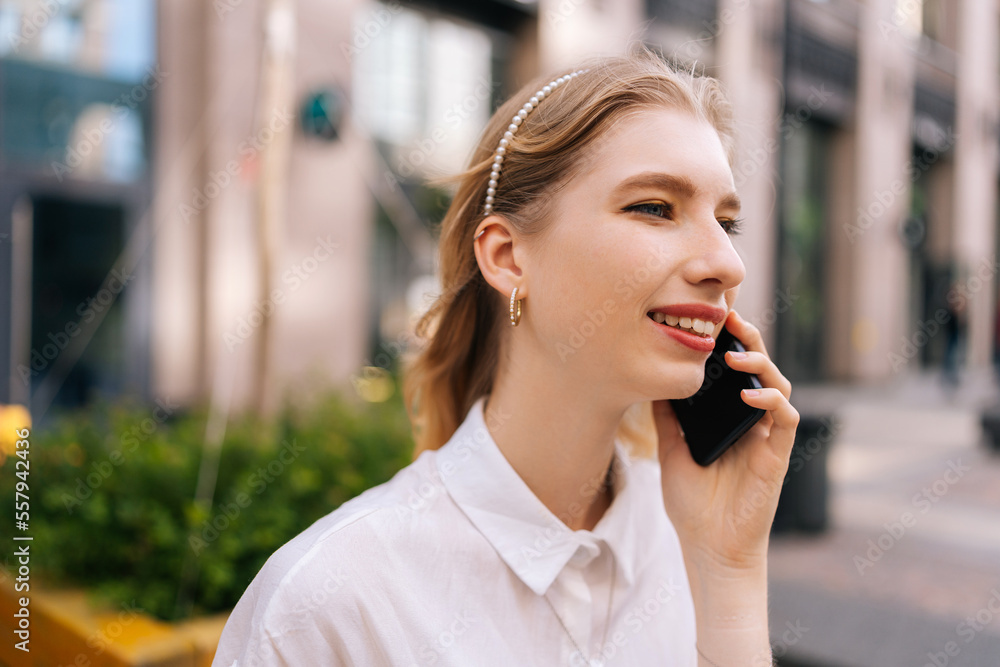 Close-up face of happy cheerful young woman talking on smartphone with friends rejoicing smiling white teeth sitting on bench on city street. Beautiful lovely lady walking outdoors, talking on phone Close-up face of happy cheerful young woman talking on smartphone with friends rejoicing smiling white teeth sitting on bench on city street. Beautiful lovely lady walking outdoors, talking on phone