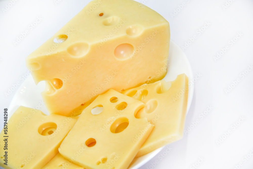 A large piece of cheese with holes on the plate. Chopped cheese and small slices on a white background. Juicy and delicious natural cheese. Cheese holes.
