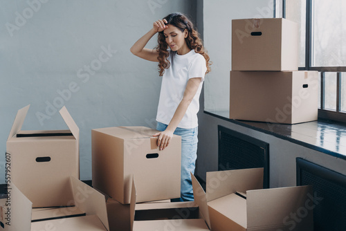 Tired woman unpacking cardboard boxes. Packing things, shipping service and relocation concept.