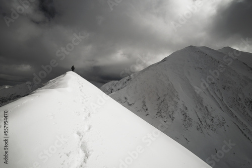 Wędrówka górska zaśnieżoną granią. Tatry polskie i słowackie. Ślady. Wędrowiec na szlaku. Zmienna pogoda z dynamicznie wyglądającymi chmurami