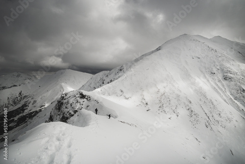 Wędrówka górska zaśnieżoną granią. Tatry polskie i słowackie. Ślady. Wędrowiec na szlaku. Zmienna pogoda z dynamicznie wyglądającymi chmurami