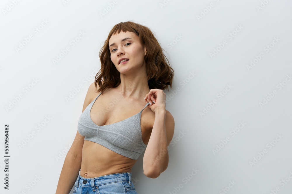 Naklejka premium a beautiful, sexy, playful woman with tanned skin color and red hair stands on a white background playfully pulling the strap of her top