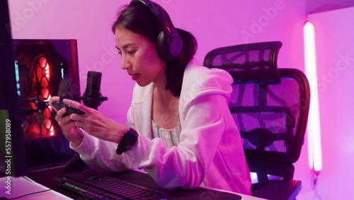 Happy asia female gamer wear headphone competition play video game online with smartphone share experience with audience neon light at night. Esport streaming game online, cybersport luiser activity. photo