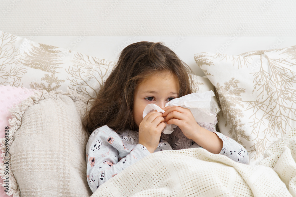 Little girl blow stuffy nose with white handkerchief. Portrait of unhealthy child. Kid in sleepwear lie under blanket and have bed rest. Home treatment. Runny nose, snot, cold symptoms, cure. Little girl blow stuffy nose with white handkerchief. Portrait of unhealthy child. Kid in sleepwear lie under blanket and have bed rest. Home treatment. Runny nose, snot, cold symptoms, cure.