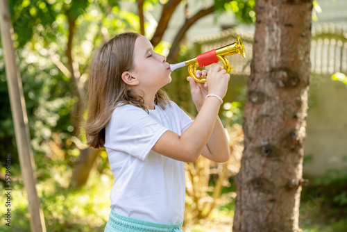 Elementary school age girl playing a toy trumpet prop  holding it in hands doing a bugle call signal. Simple calling  call to arms  signalling abstract concept. Children and music education  sounds