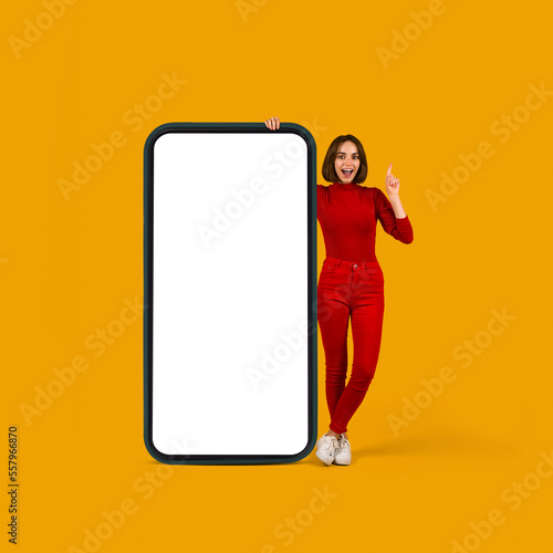 Excited pretty young woman posing by huge cell phone, mockup